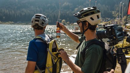 Kolmnock and two trail adventures © David Karg Two cyclists by the lake, one holding a beer bottle and opening a backpack