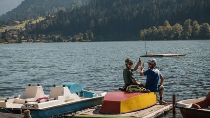 The Millstätter See cycle path © David Karg Two cyclists on dock at lake with mountains in background toasting bottles