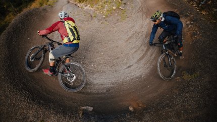 Flow & Nature Signature Trail Tour (incl. cable car) © David Karg Two mountain bikers riding on a gravel trail with a sharp curved turn