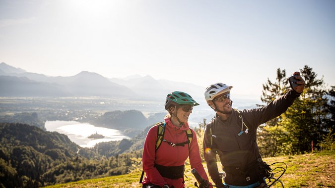 Mountain Bike Holidays © Bled - Samo Vidic Zwei Fahrradfahrer machen Selfie mit Berg- und Seeblick im Hintergrund