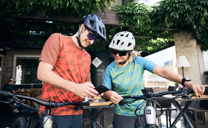 Mountain bike holiday in Brixen © Tobias Köhler Two cyclists checking a smartphone outside a café