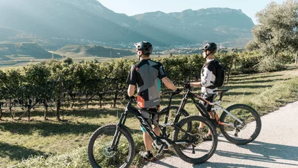NATURAL PHENOMENON ICE HOLES © Fabian Pomella Two cyclists with mountain bikes overlooking vineyards and mountains in sunlight