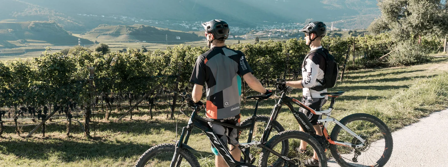 NATURAL PHENOMENON ICE HOLES © Fabian Pomella Two cyclists with mountain bikes overlooking vineyards and mountains in sunlight
