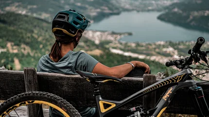 2 LAKES TOUR © Andrea Acler Woman with bike helmet sitting on bench overlooking lake and mountains