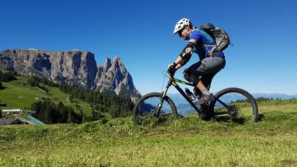 PANORAMA AND RELAX E-BIKE - VAL GARDENA VALLEY TOUR © Hotel Digon St. Ulrich Man mountain biking on grassy hill with rocky mountains in background