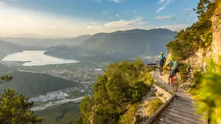 Kaiserjäger single trail © WOM Medien - Andreas Meyer Two mountain bikers ride a trail overlooking a valley and lake