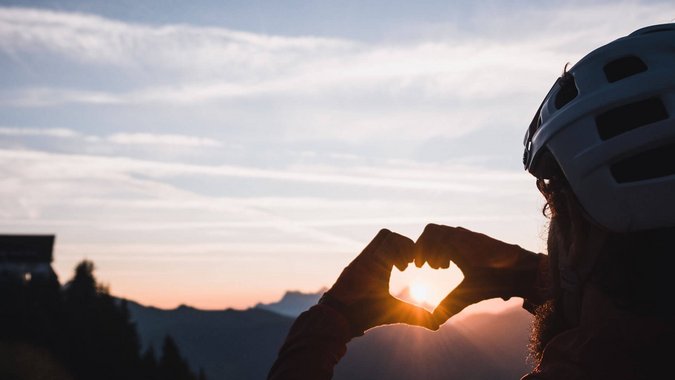 Mountain Bike Holidays © Norman Bielig Fahrradfahrer formt Herz mit Händen vor dem Sonnenuntergang in den Bergen