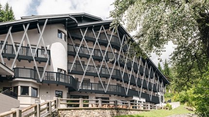 Hotel Arpuria | Hidden Luxury Mountain Home © Brandnamic Modernes mehrstöckiges Gebäude mit Balkonen und Holzgitterstruktur in grüner Landschaft
