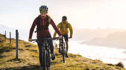 ASCHAUER HÖHENWEG © TVB Kitzbüheler Alpen Brixental - Mathäus Gartner Two people mountain biking on a mountain trail in sunlight