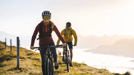 ASCHAUER HÖHENWEG © TVB Kitzbüheler Alpen Brixental - Mathäus Gartner Two people mountain biking on a mountain trail in sunlight