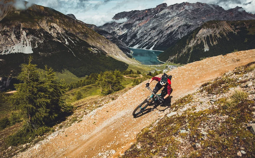Mountain bike holidays in Livigno © Livigno - Ezequiel Urrets Mountain biker riding on mountain trail with lake and mountains behind
