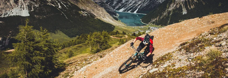 Livigno © Livigno - Ezequiel Urrets Mountain biker riding on mountain trail with lake and mountains behind