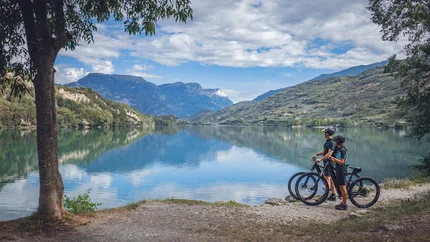 Cavedine Valley © APT Garda Dolomiti Two cyclists stand by lake looking at mountains and sky