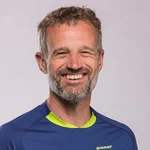 Mountain Bike Holidays © WOM Medien Mann lächelt in blau-grünem Mountainbike-Trikot vor grauem Hintergrund