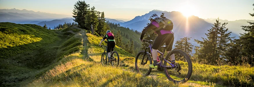 Flachau © Salzburger Sportwelt - Andreas Meyer Two mountain bikers riding on a mountain trail at sunset