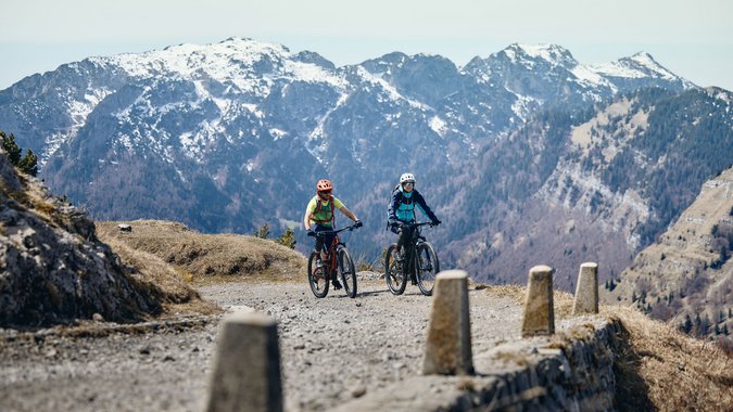 Mountain Bike Holidays © Tobias Köhler Zwei Radfahrer fahren auf bergigem Weg mit schneebedeckten Bergen im Hintergrund