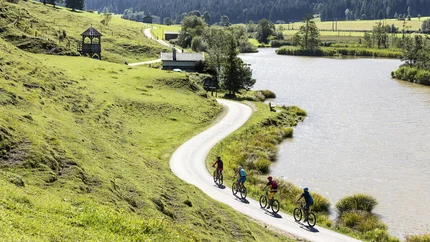 Panorama - Steinberg Tour © Saalfelden Leogang Touristik Four cyclists riding on a path beside a lake in hilly countryside