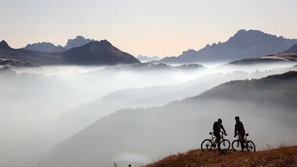 5 TORRI © Davide dal Mas Two mountain bikers on a hill with foggy mountains in the background