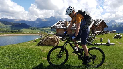 SEISERALM AND JENDER VALLEY © Hotel Digon St. Ulrich Cyclist with helmet near mountain huts and lake under sunny sky