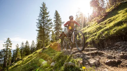 Tschengla Unchained © Michael Marte - Bikepark Brandnertal Two people mountain biking on rocky forest trail in sunlight