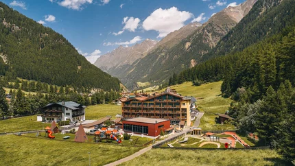 Hotel Sunny Sölden © Christian Schneider Photography Blick auf ein Dorf mit Spielplatz in einem grünen Tal zwischen bewaldeten Bergen
