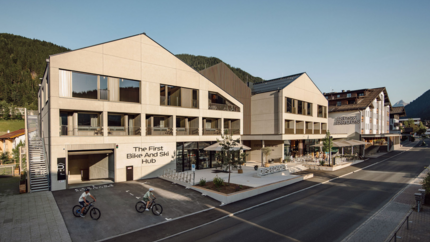 Dips&Drops - HOTEL · SPORTS · SPA · RESTAURANTS © Matthias Warter Modern building with bike and ski hub and two cyclists outside