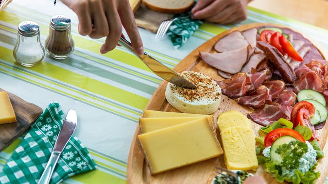 Mountain Bike Holidays © David Karg Messer schneidet Käse auf einer Platte mit verschiedenen Käsesorten und Wurst