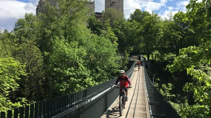 Castles Tour © Hotel Innerhofer Cyclists crossing a suspension bridge with a castle in a lush green forest