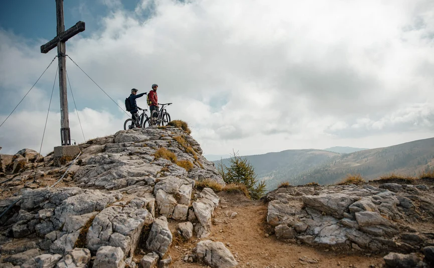 Mountain Bike holidays in the Weissensee region © David Karg Two mountain bikers on rocky summit next to cross in the mountains