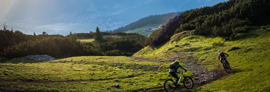 Tiroler Zugspitz Arena © Norman Bielig Two mountain bikers riding on a mountain trail at sunrise