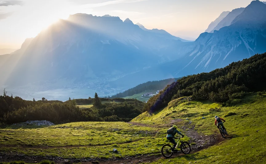 Mountain bike holidays in the Tiroler Zugspitz Arena © Norman Bielig Two mountain bikers riding on a mountain trail at sunrise