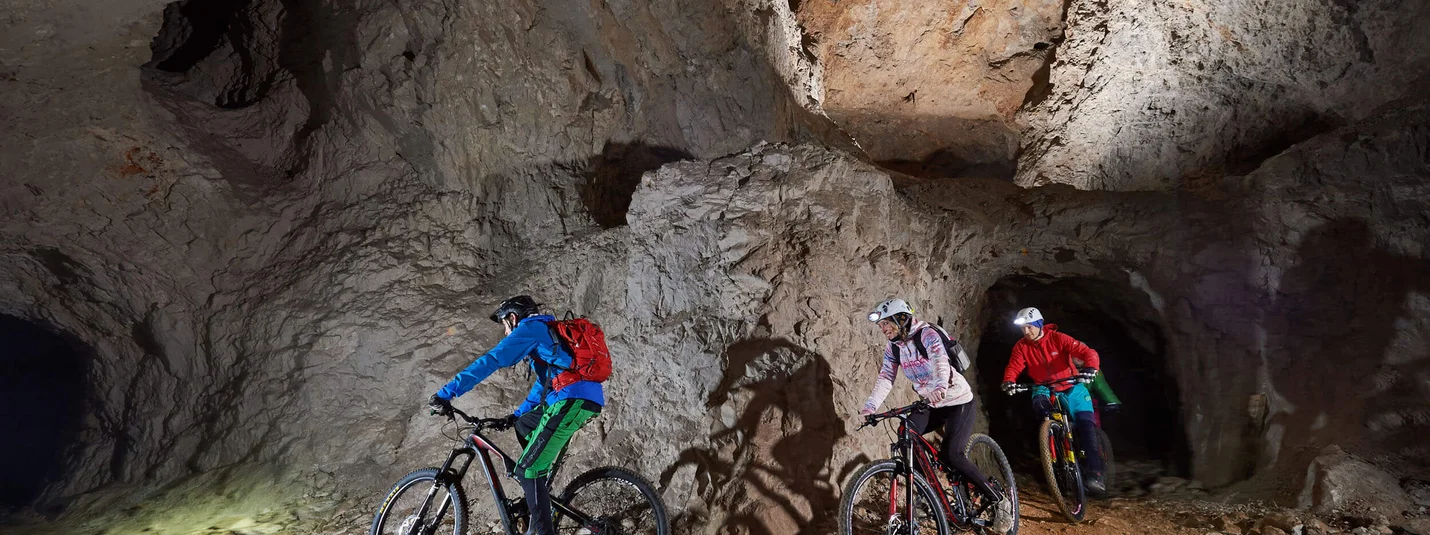 UNDERGROUND BIKING TOUR © Tomo Jesenicnik Three mountain bikers riding in a lit cave tunnel