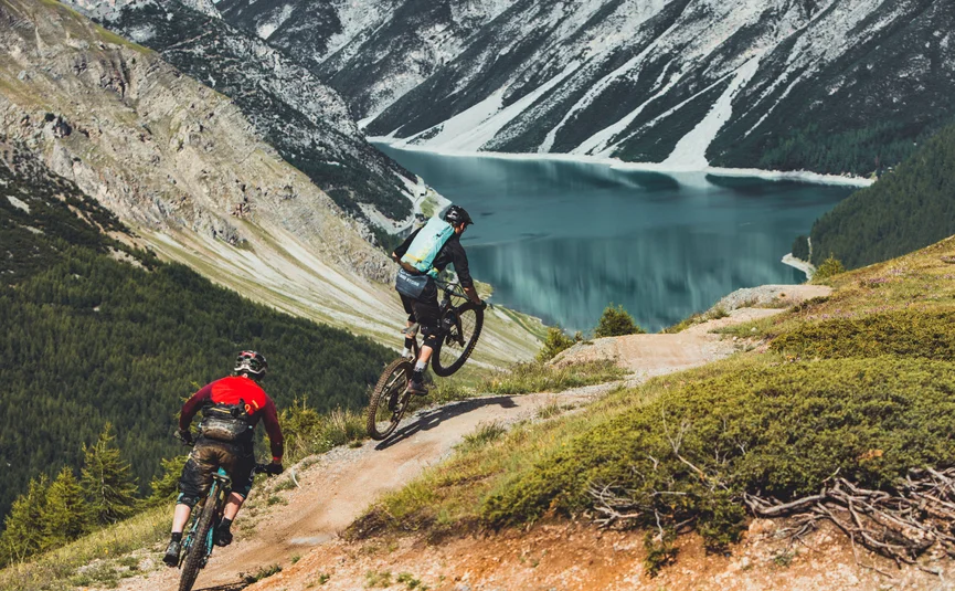 Mountain bike holidays in Livigno © Livigno - Ezequiel Urrets Two mountain bikers riding on a mountain trail overlooking a lake