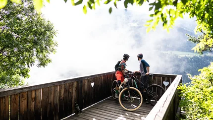 Brixen Tour © Hotel Jonathan Two mountain bikers on a wooden viewpoint overlooking a foggy valley