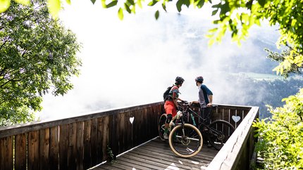 Brixen Tour © Hotel Jonathan Two mountain bikers on a wooden viewpoint overlooking a foggy valley