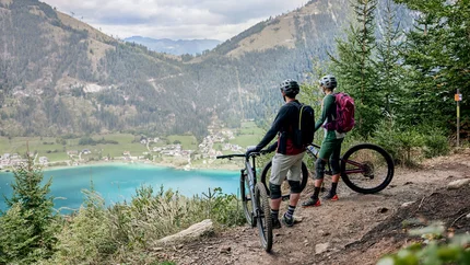 Carinthia © Tobias Köhler Two mountain bikers overlooking a lake and mountains from a forest trail