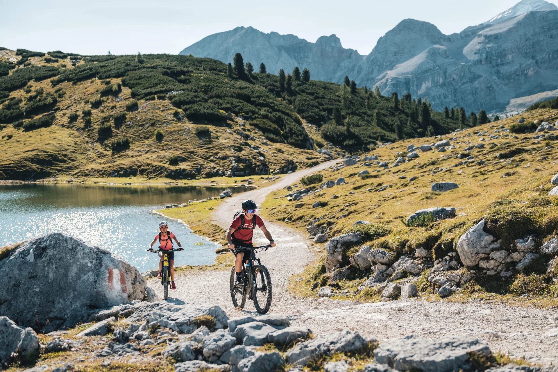 Mountain Bike Holidays © Alex Moling Zwei Mountainbiker fahren auf einem bergigen Wanderweg neben einem See