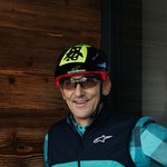 Mountain Bike Holidays © Ziga Intihar Radfahrer mit Helm und Handschuhen zeigt Daumen vor beleuchtetem G auf Holzwand