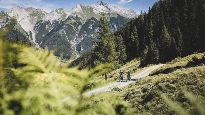 Mountain Bike Holidays © TVB St. Anton am Arlberg - Patrick Bätz Zwei Radfahrer auf Waldweg mit Bergpanorama im Hintergrund