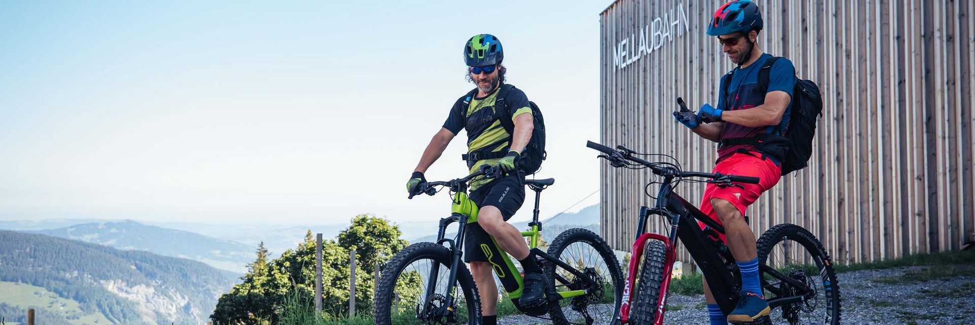 Alpen Hotel Post **** © Bregenzerwald Tourismus - Sebastian Stiphout Two mountain bikers with helmets next to MellauBahn building in the mountains