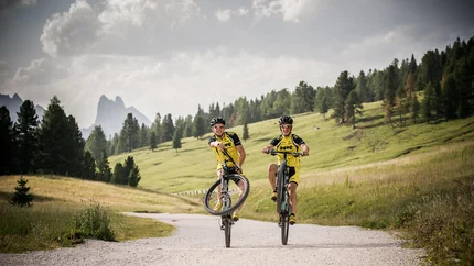 THROUGH THE SEXTNER VALLEY TO THE HUT AT THE END OF THE VALLEY © Harald Wisthaler Two cyclists doing wheelies on a gravel path in the mountains