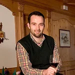 Mountain Bike Holidays © Hotel Digon St. Ulrich Mann sitzt auf Weinfass mit Weinflaschen und Glas in gemütlichem Raum