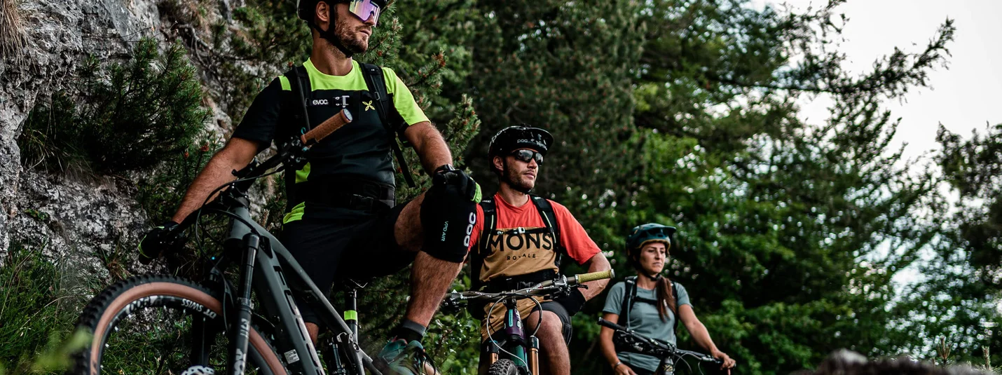 SENTIERO DELLA PACE © Andrea Acler Drie mountainbikers met helmen rusten op rotsachtig pad in bos