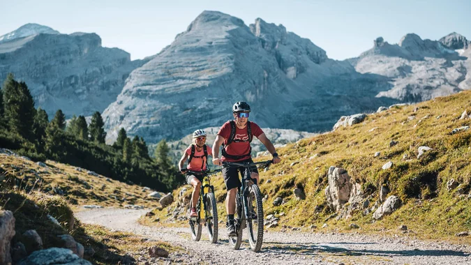 Mountain Bike Holidays © Alex Moling Zwei Mountainbiker fahren auf einem Bergweg vor großen Bergen