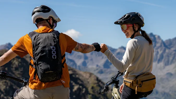 Mountain Bike Holidays © TVB Paznaun – Ischgl Zwei Mountainbiker mit Helm geben sich auf Berglandschaft die Faust