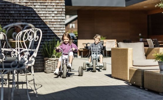 Familienurlaubswoche Zwei Kinder fahren mit Dreirädern auf einer Terrasse in sonnigem Außenbereich