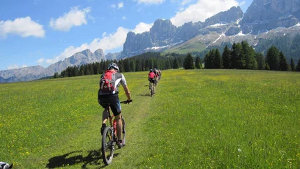 GRAND ROSE GARDEN TOUR © Exploring GmbH Group mountain biking on green meadow with forested mountains and blue sky