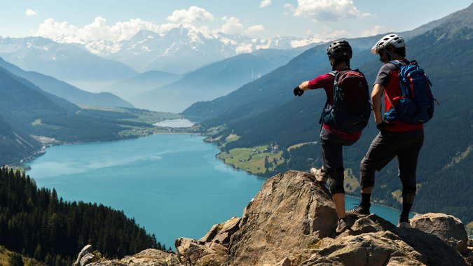 Mountain Bike Holidays © David Karg Zwei Wanderer mit Rucksäcken auf Felsen über blauem Bergsee