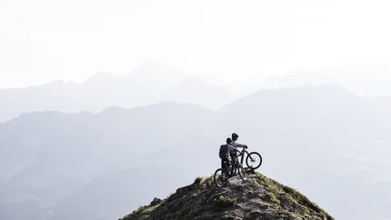 Diedamskopf - Neuhornbach © Alpen Hotel Post Two mountain bikers on a peak with misty mountain ranges in the background