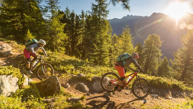 Mountain Bike Holidays © WOM Medien - Andreas Meyer Zwei Mountainbiker fahren auf einem Waldweg mit Sonnenuntergang